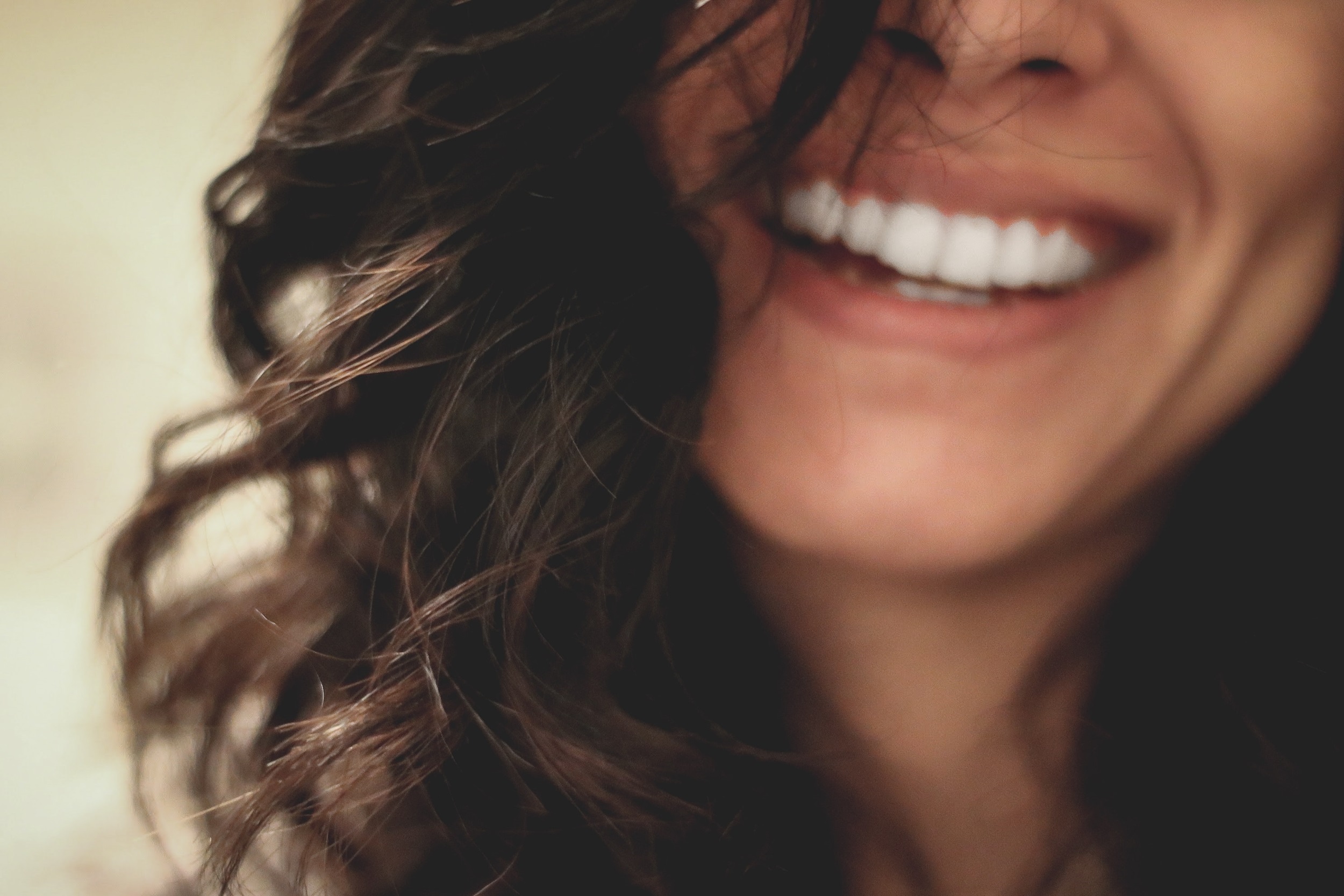 A focused image of a woman with brunette hair smiling with bright white teeth